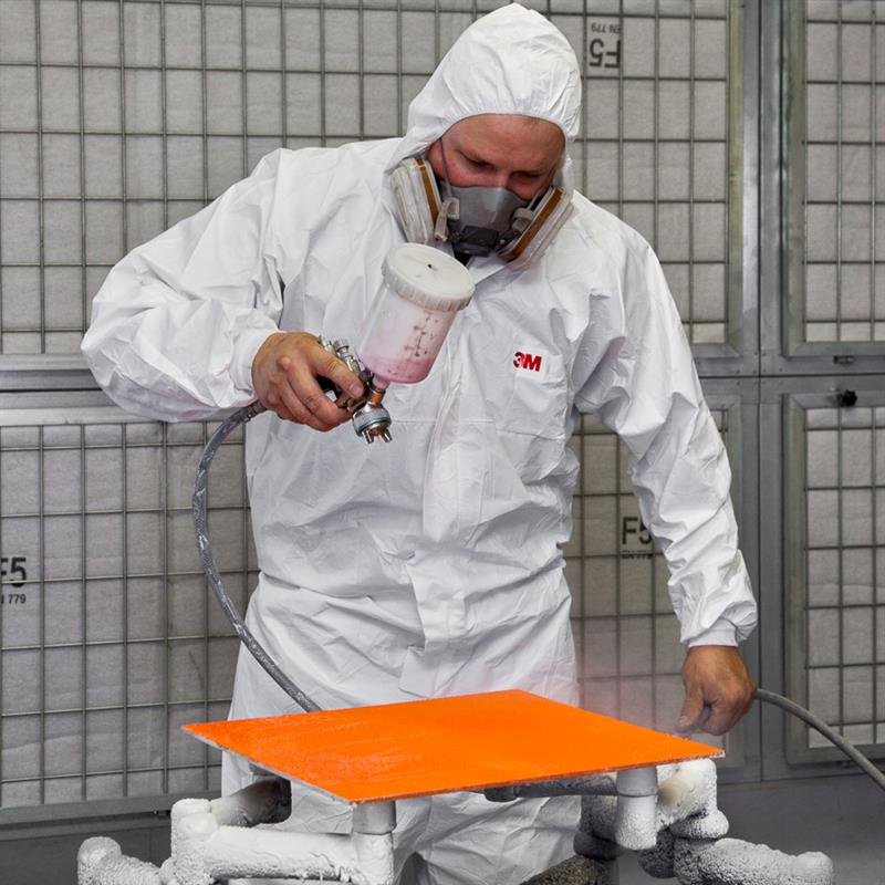 Mitarbeiter im Schutzanzug lackiert ein Möbelteil in der Lackierkabine