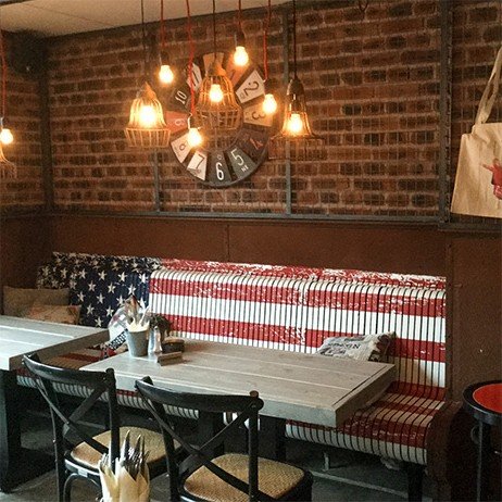 Sitzbank mit Flaggenmotiv, Holztische und Industrieleuchten in einem Restaurant
